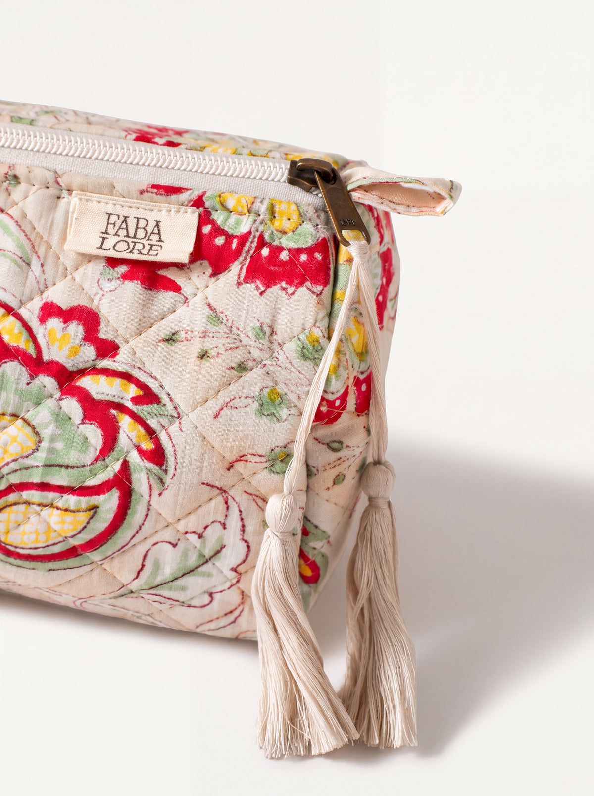 Close up of Fabalore Meadow quilted pouch showing floral fabric, zipper, logo label and cream tassels.