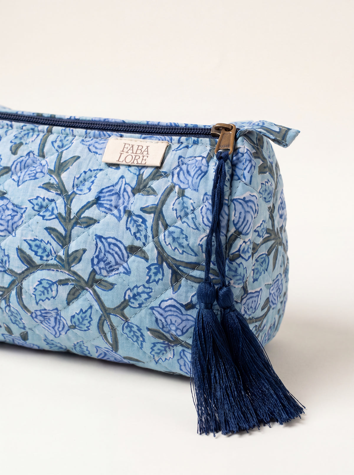 Close-up of Fabalore Blue Bloom quilted pouch showing floral fabric, zipper, logo label and navy tassels.