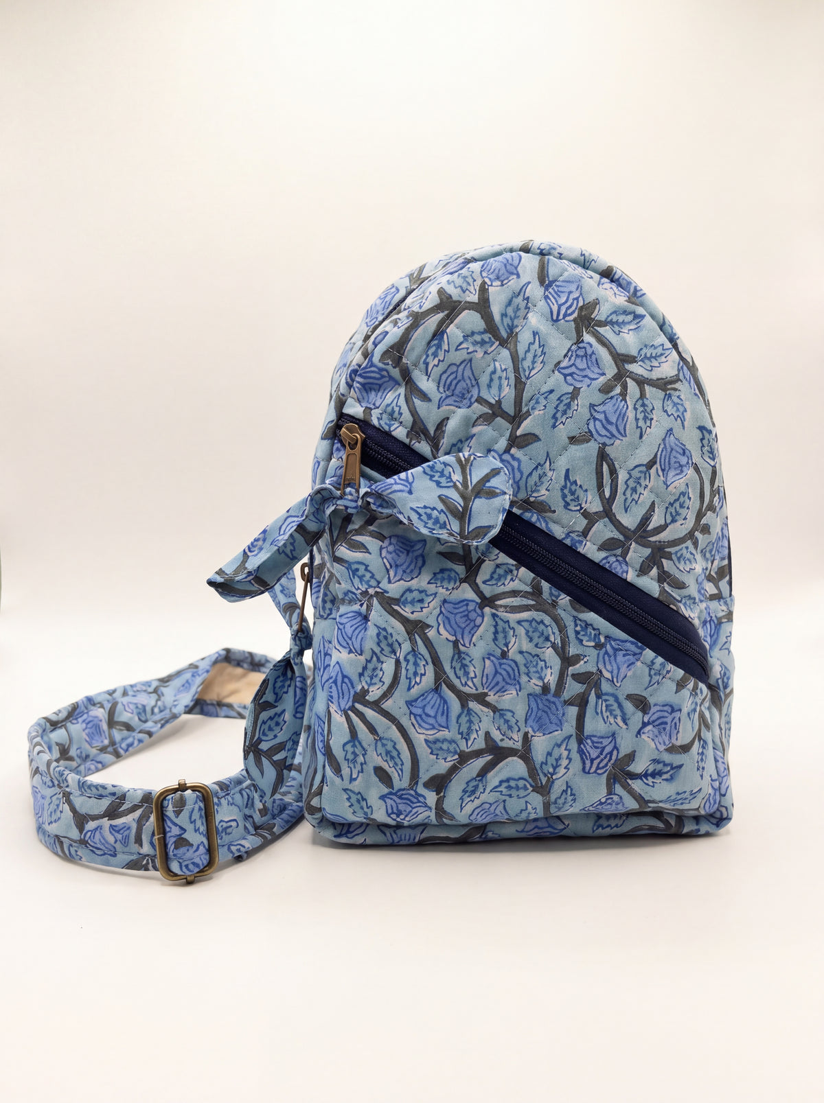 Fabalore Blue Bloom quilted sling backpack with blue floral print, front zip pocket and adjustable strap.