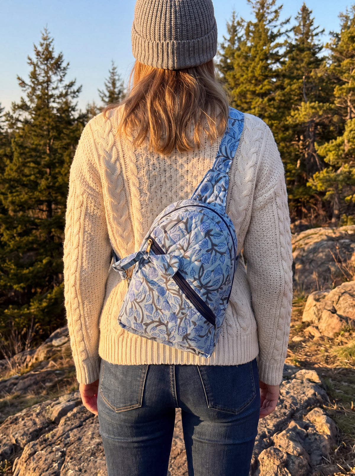 Woman wearing the Blue Bloom quilted sling backpack across her back with the adjustable strap visible.