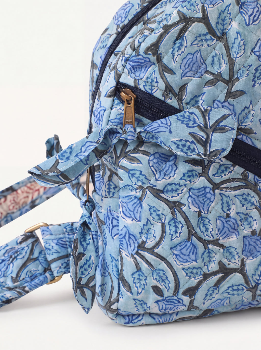 Close up of Blue Bloom quilted sling backpack showing floral fabric, front zipper and fabric bow detail.