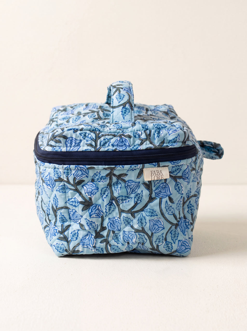 Blue Bloom quilted floral vanity case showing structured shape, top handle and navy zip-around closure.