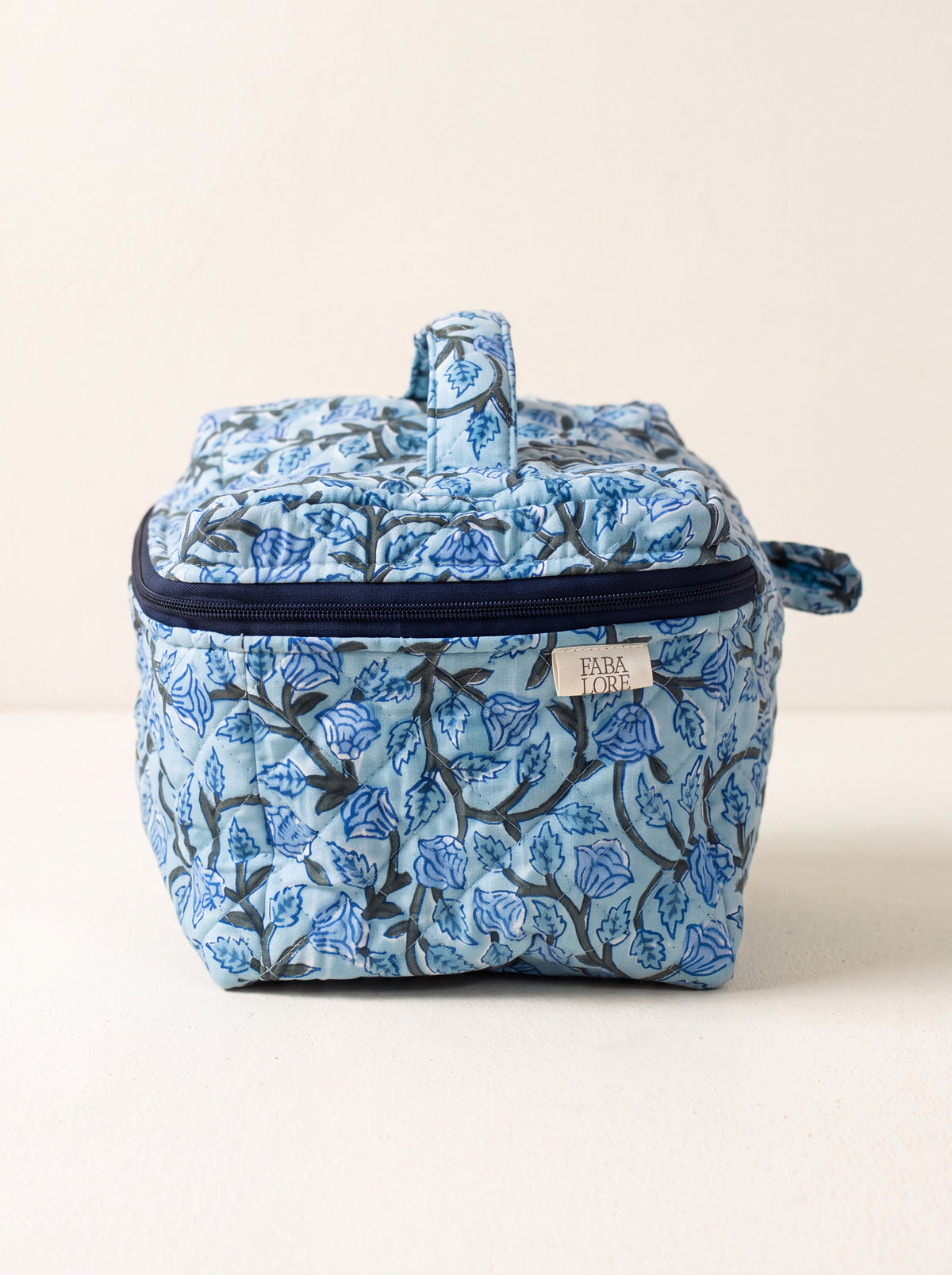 Blue Bloom quilted floral vanity case showing structured shape, top handle and navy zip-around closure.