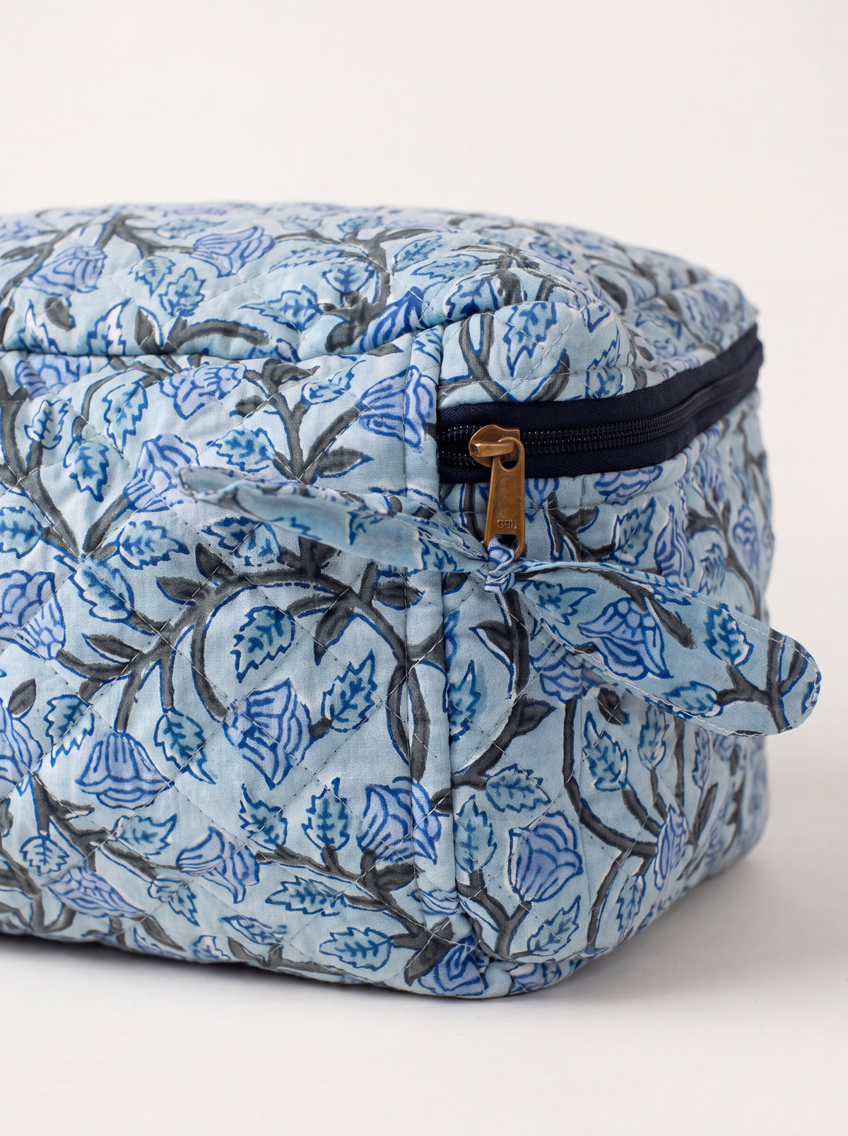 Close up of Fabalore Blue Bloom vanity case showing quilted floral fabric, navy zipper and fabric zipper pull.