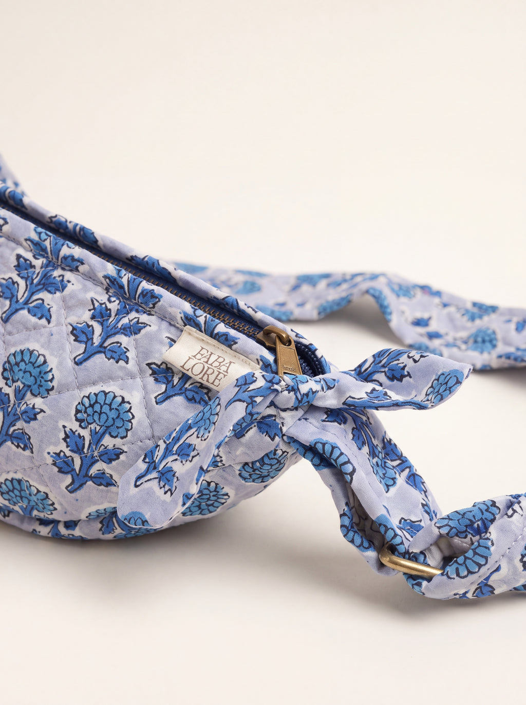 Close up of Fabalore Indigo Bloom sling bag showing floral fabric, zipper, logo label and strap hardware.