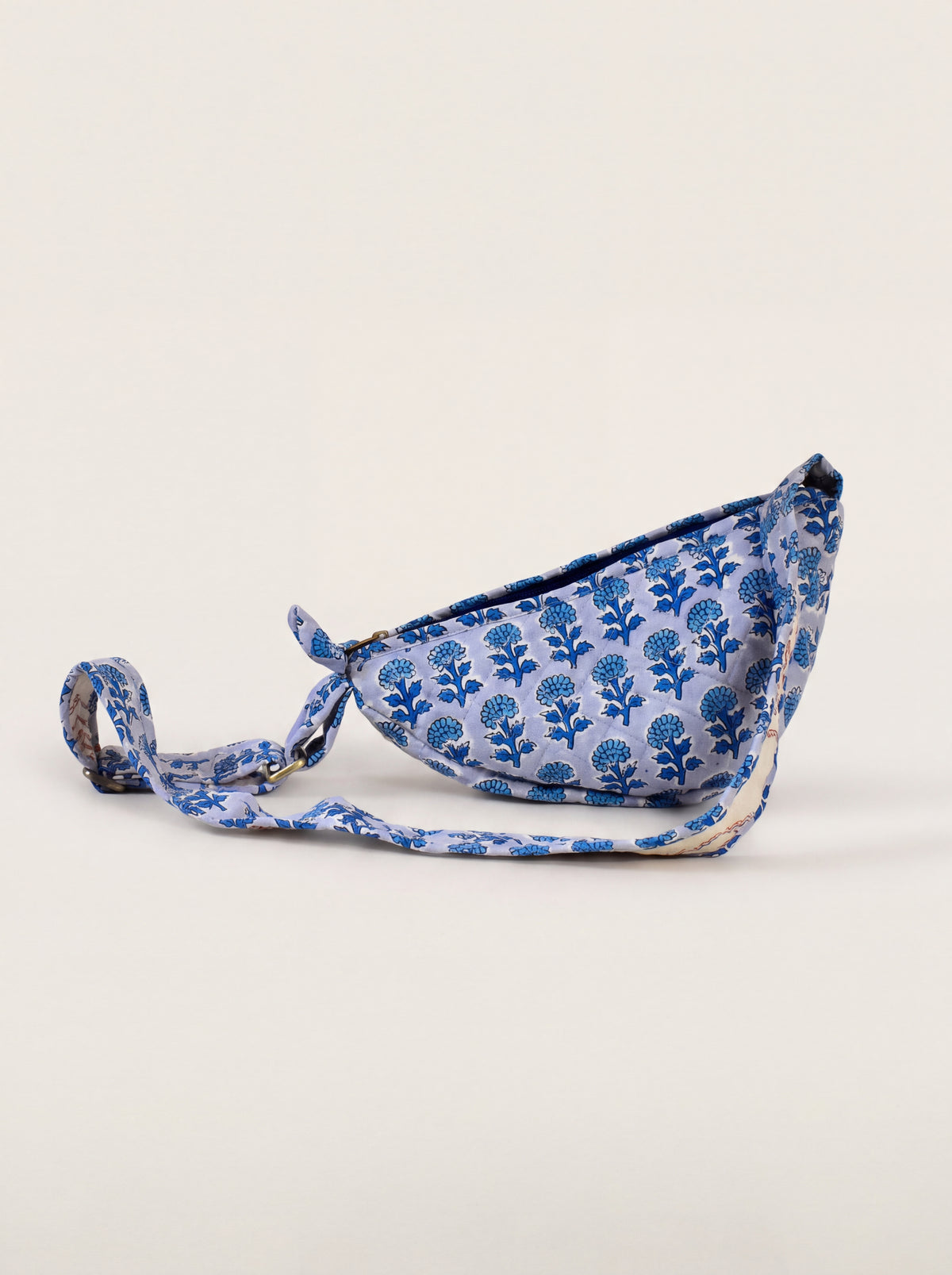 Indigo Bloom quilted floral sling bag showing curved shape and adjustable printed strap.