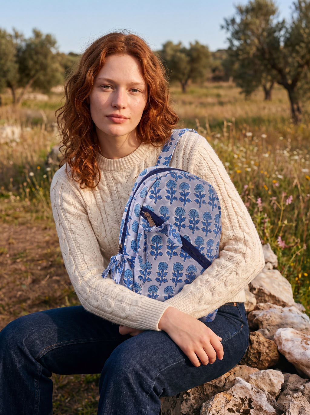 Woman seated outdoors holding the Fabalore Indigo quilted backpack in a blue floral print.