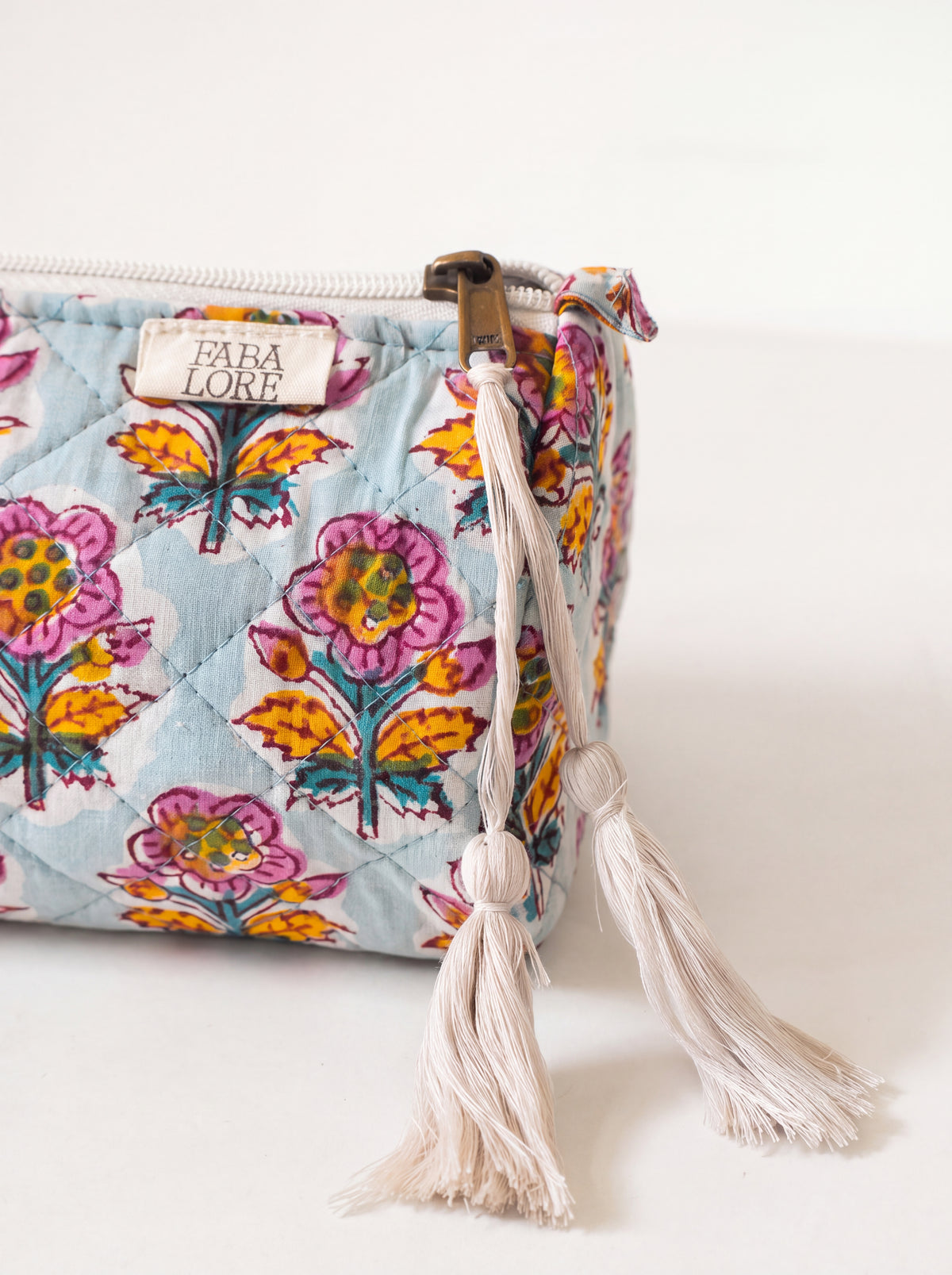 Close up of Fabalore Marigold Bloom quilted pouch showing floral fabric, zipper, logo label and cream tassels.