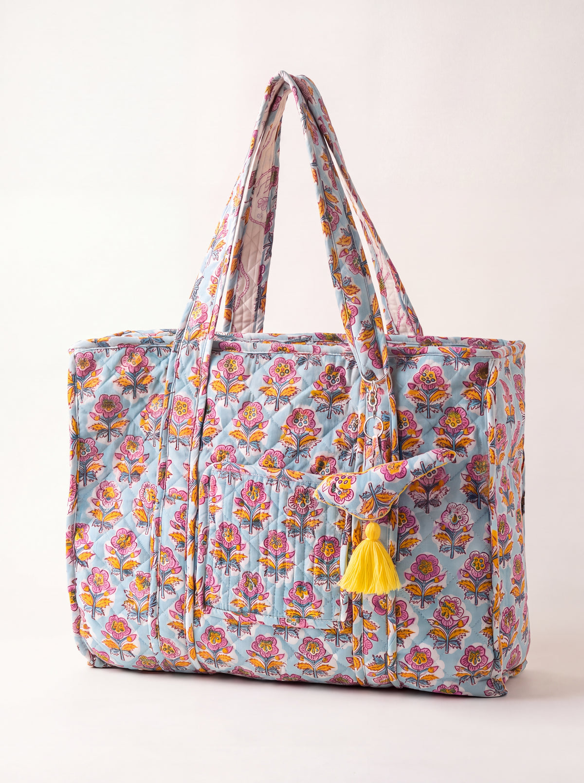 Fabalore Marigold Bloom quilted tote bag with light blue floral print, exterior pockets, shoulder straps and yellow tassel.