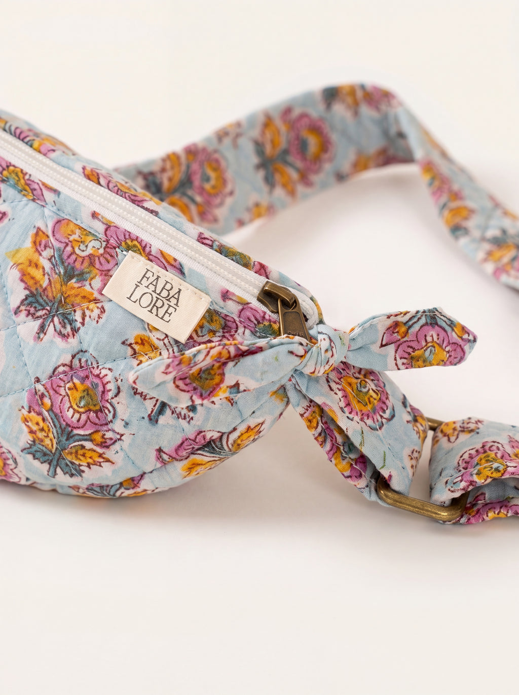 Close up of Fabalore Marigold Bloom sling bag showing floral fabric, zipper, logo label and strap hardware.