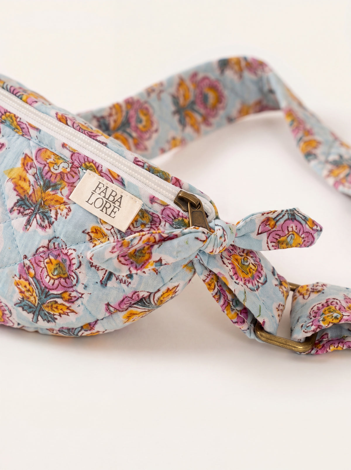 Close up of Fabalore Marigold Bloom sling bag showing floral fabric, zipper, logo label and strap hardware.