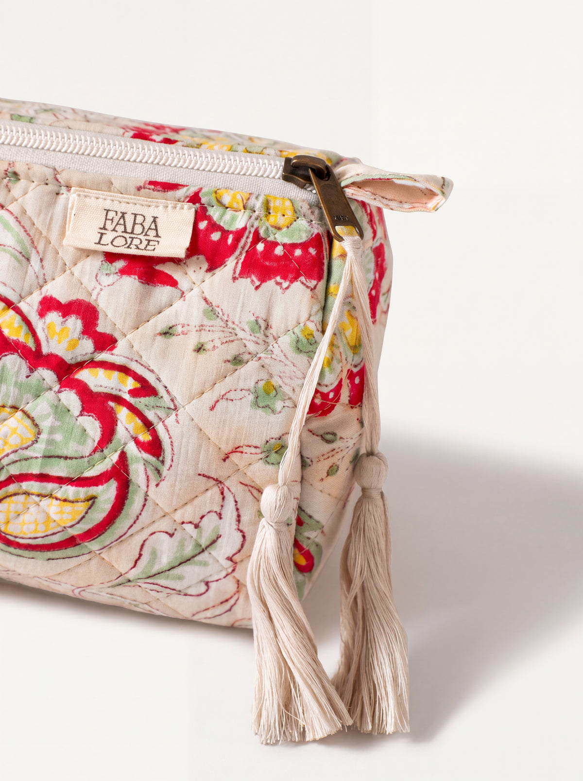 Close-up of Fabalore Meadow quilted pouch showing floral fabric, zipper, logo label and cream tassels.