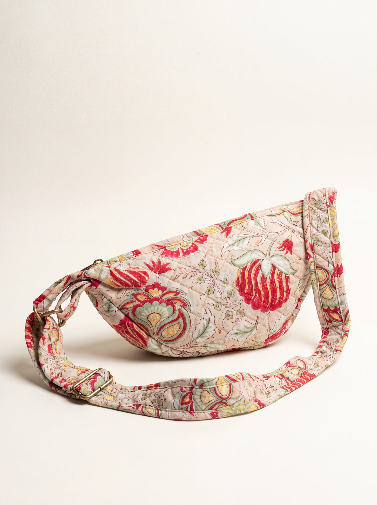 Floral quilted crossbody sling bag with full adjustable fabric strap and antique brass-tone hardware.