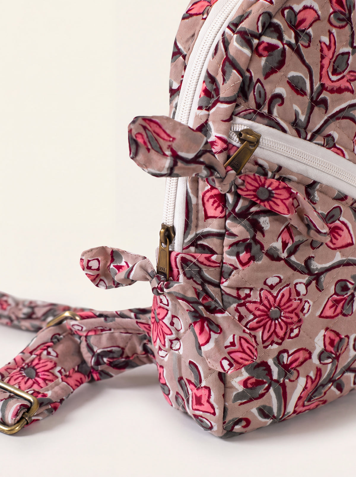 Close up of Rosewood quilted backpack showing floral print, zipper hardware, and fabric tie detail.