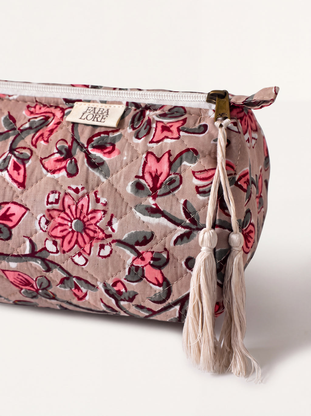 Close-up of Fabalore Rosewood quilted pouch showing floral fabric, zipper, logo label and cream tassels.