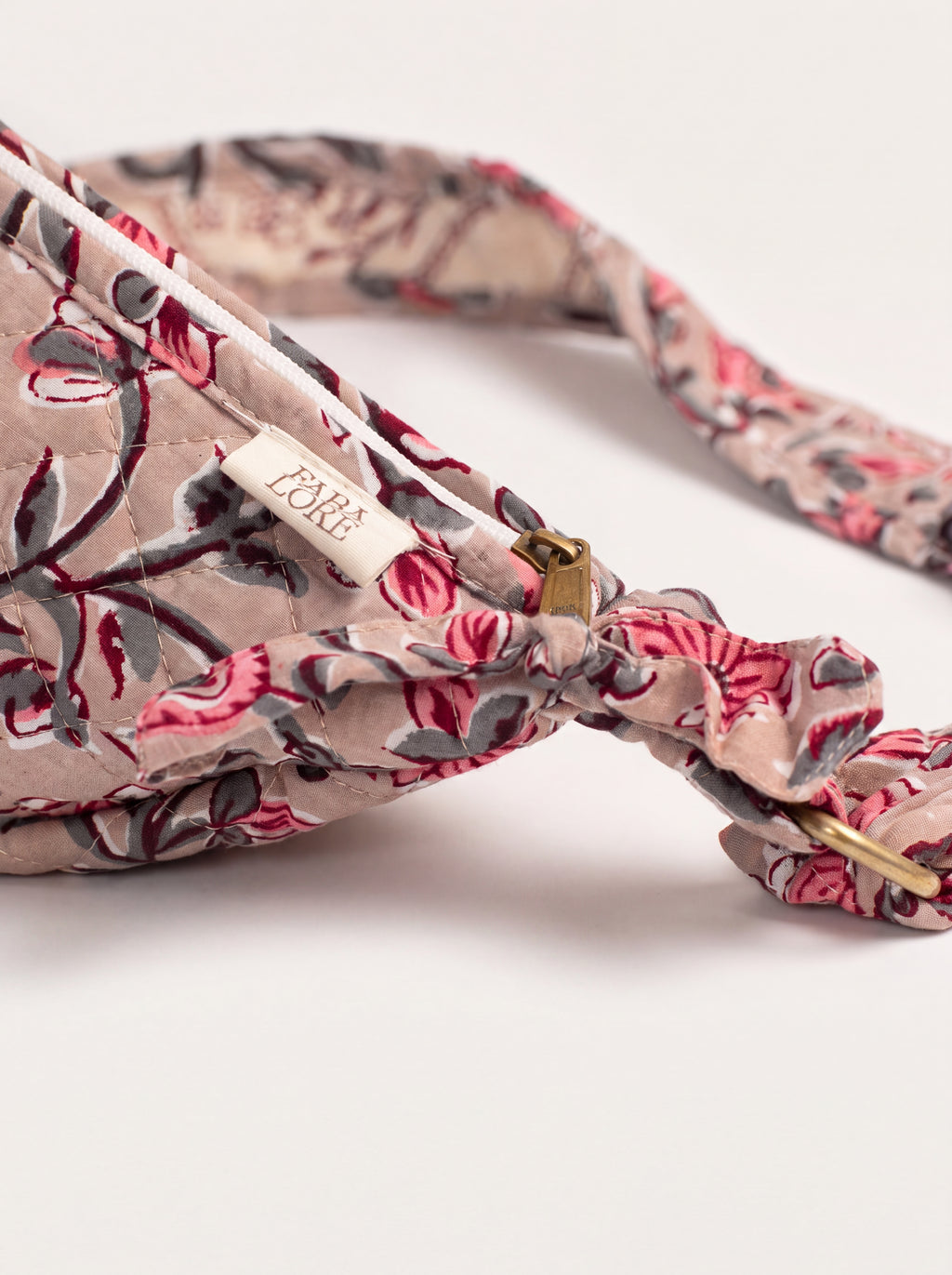 Close up of Fabalore Rosewood sling bag showing floral fabric, zipper, logo label and strap hardware.